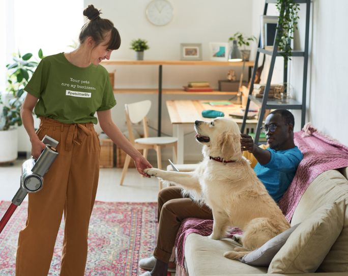 Pet sitter holding vacuum stands in front of dog and owner on couch