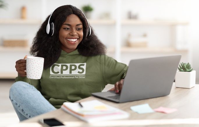 Young woman wearing a Certified Professional Pet Sitter sweatshirt sits at desk working on laptop.